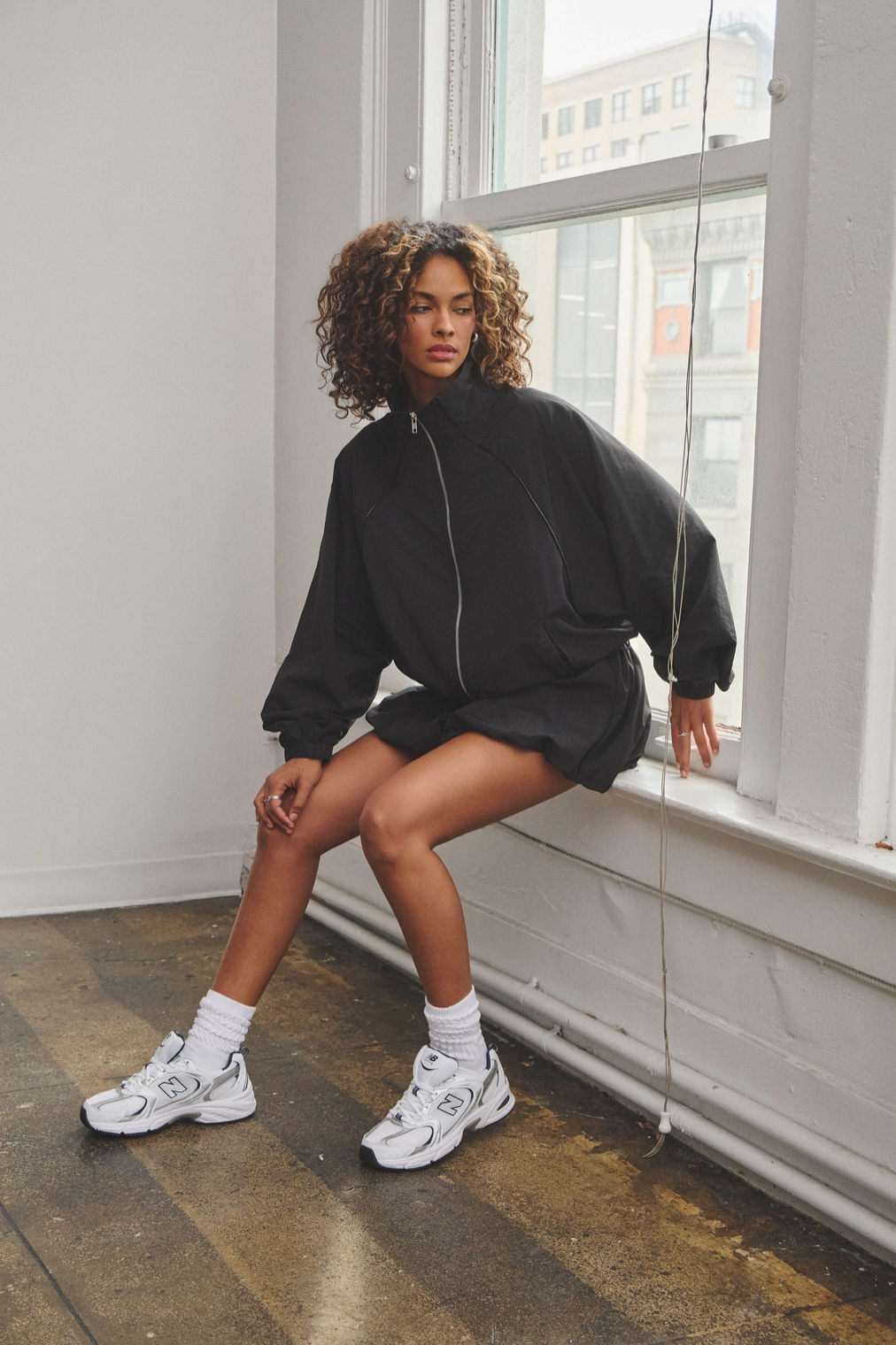 A female model wearing a black zip-up track jacket and a matching bubble mini skort with an adjustable drawstring.