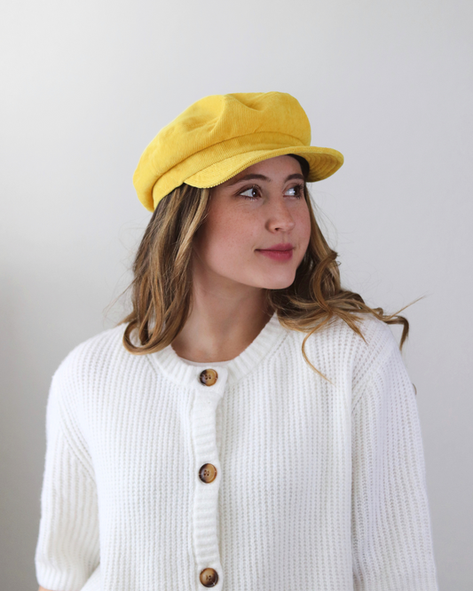 Woman wearing a yellow cap and white cardigan with brown buttons against a plain background