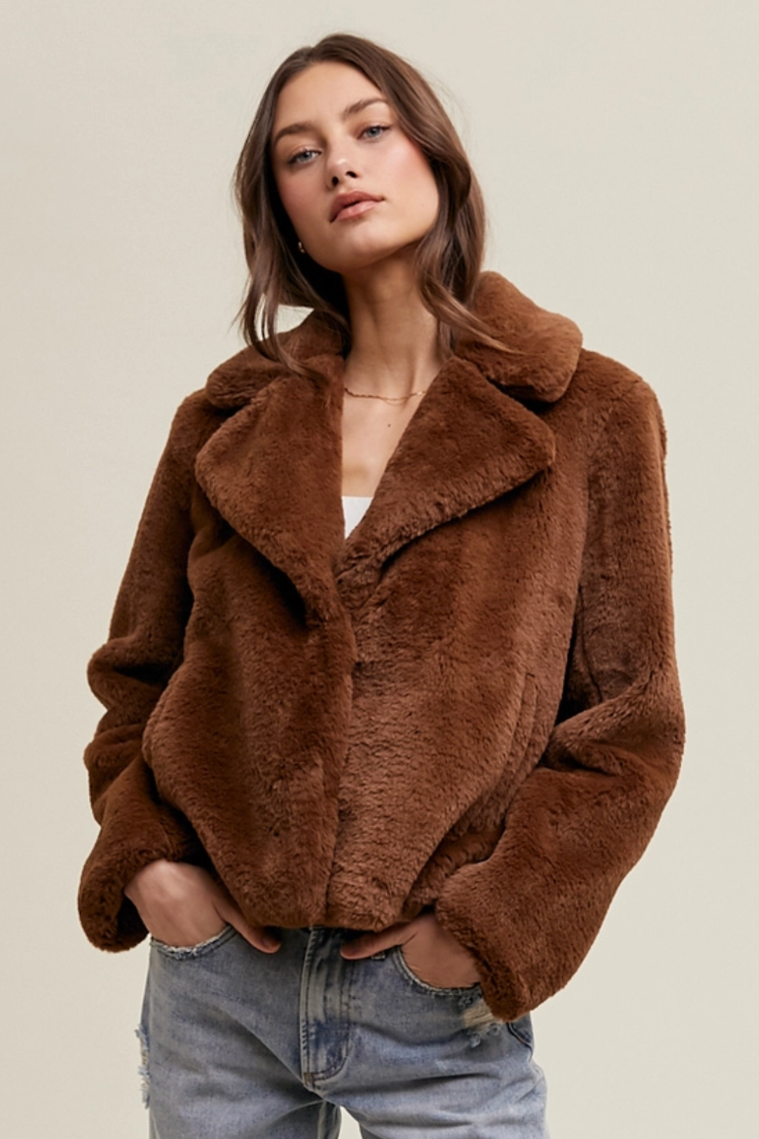 A woman wearing a brown faux fur jacket with functional buttons and side pockets, paired with blue jeans.