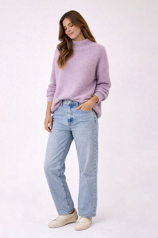 Woman wearing a lavender sweater and light blue jeans on a white background