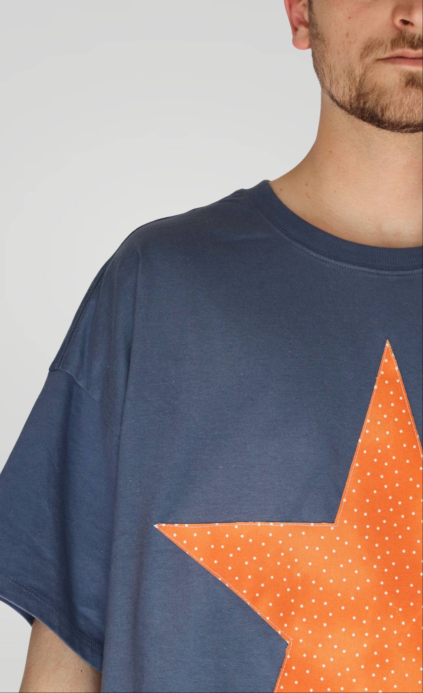 Person wearing a blue t-shirt with an orange star design on a plain background