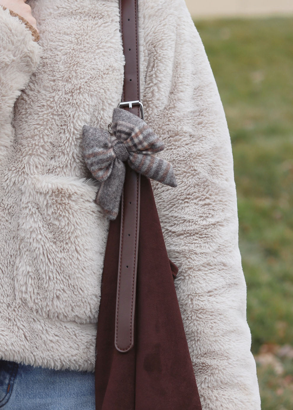 Close-up of a person wearing a fluffy coat with a plaid bow and a brown belt, standing outdoors.
