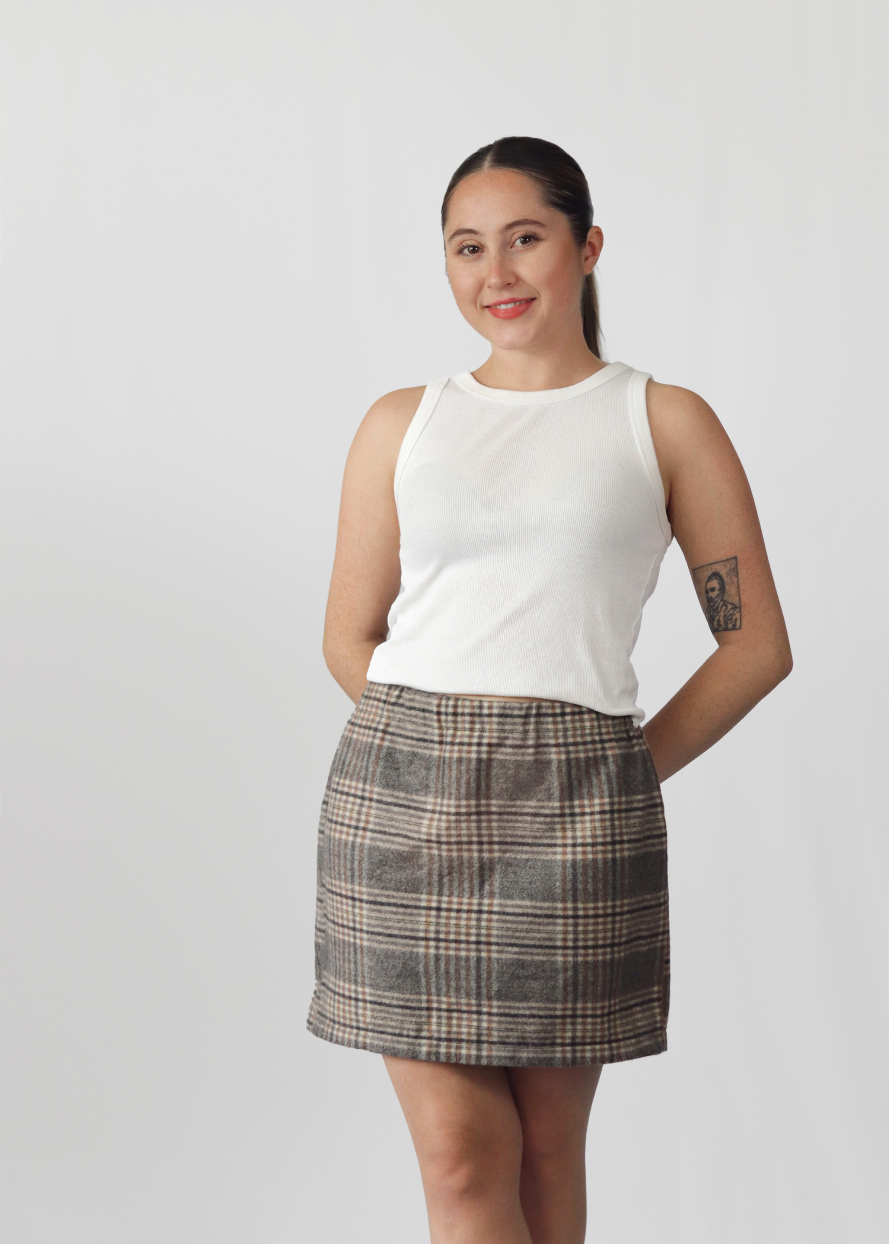 Woman wearing a white sleeveless top and plaid skirt on a plain background