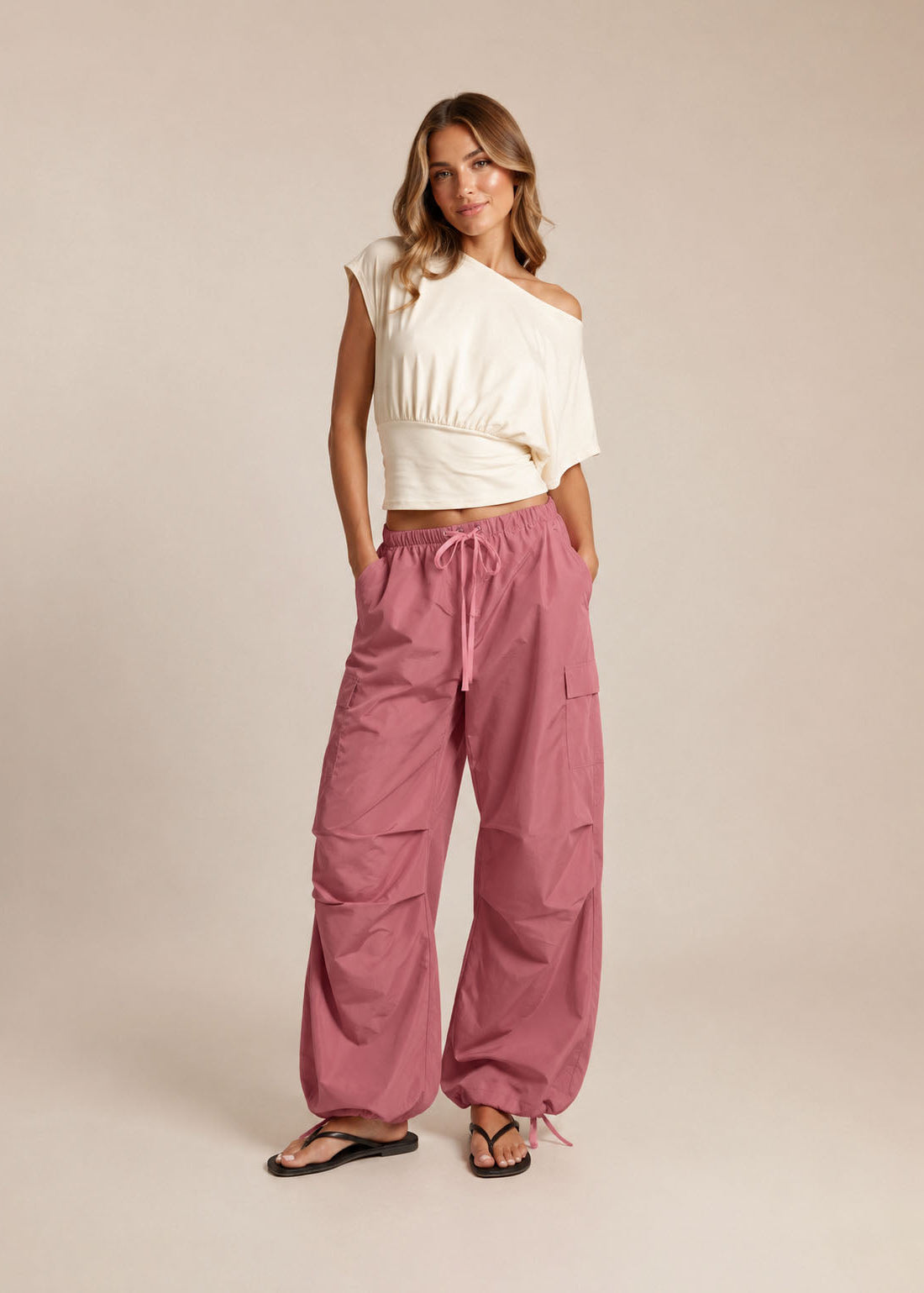 Woman wearing a white top and pink cargo pants on a beige background