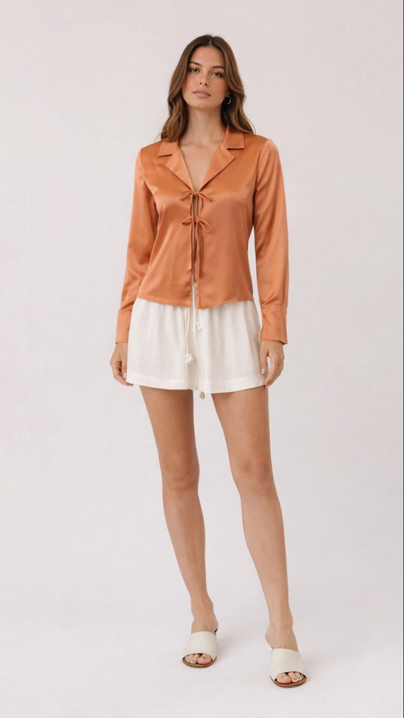 Woman wearing a peach-colored blouse and white shorts on a white background
