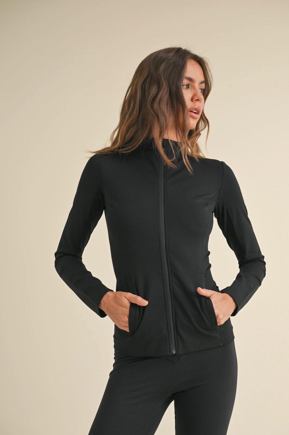 Woman wearing a black zip-up jacket on a beige background