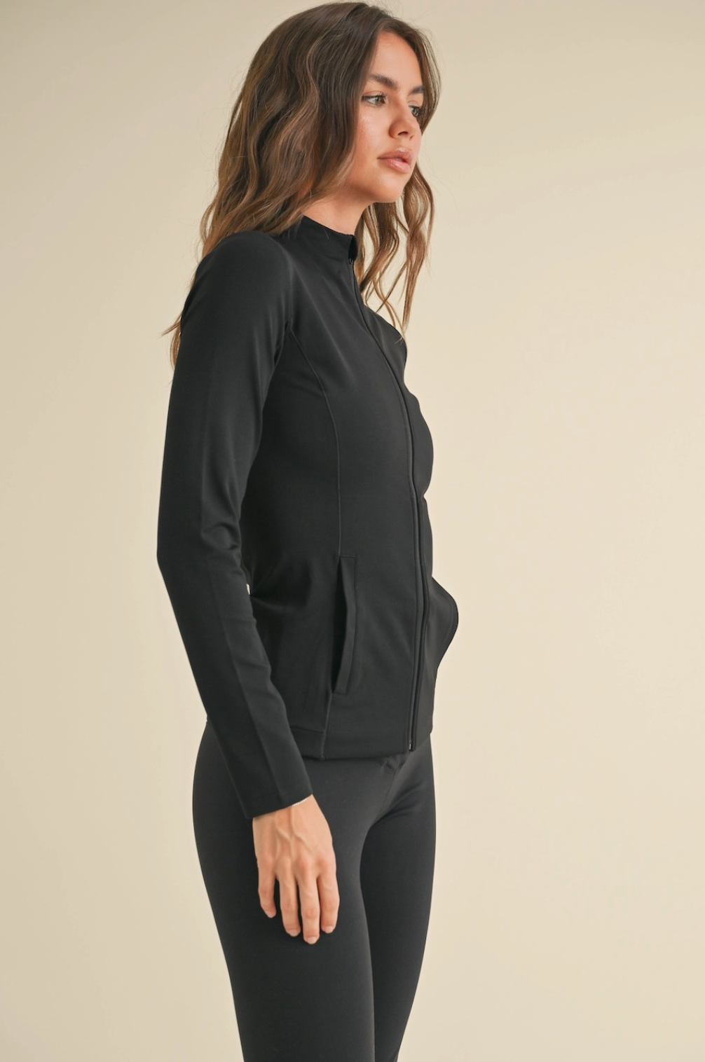 Woman wearing a black long-sleeve top and leggings on a beige background