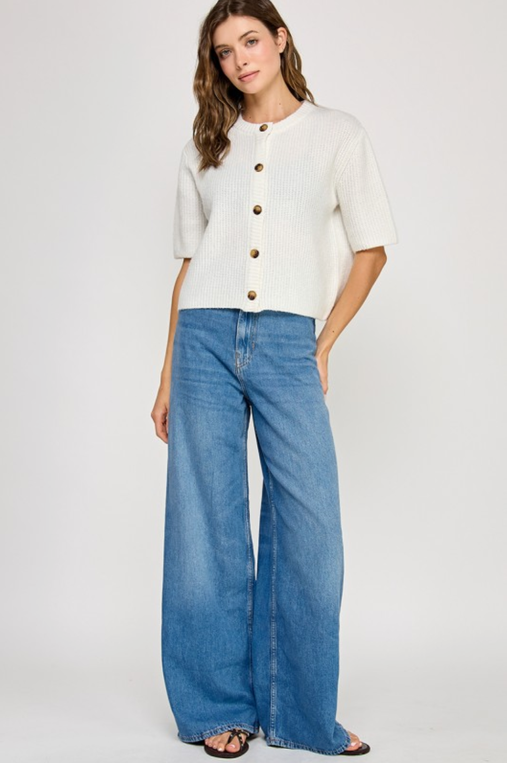 Woman wearing a white button-up shirt and blue jeans on a plain background