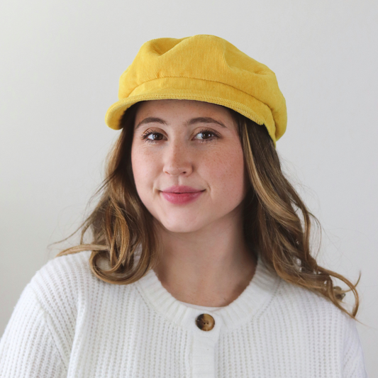 Woman wearing a yellow cap and white cardigan with brown buttons against a plain background