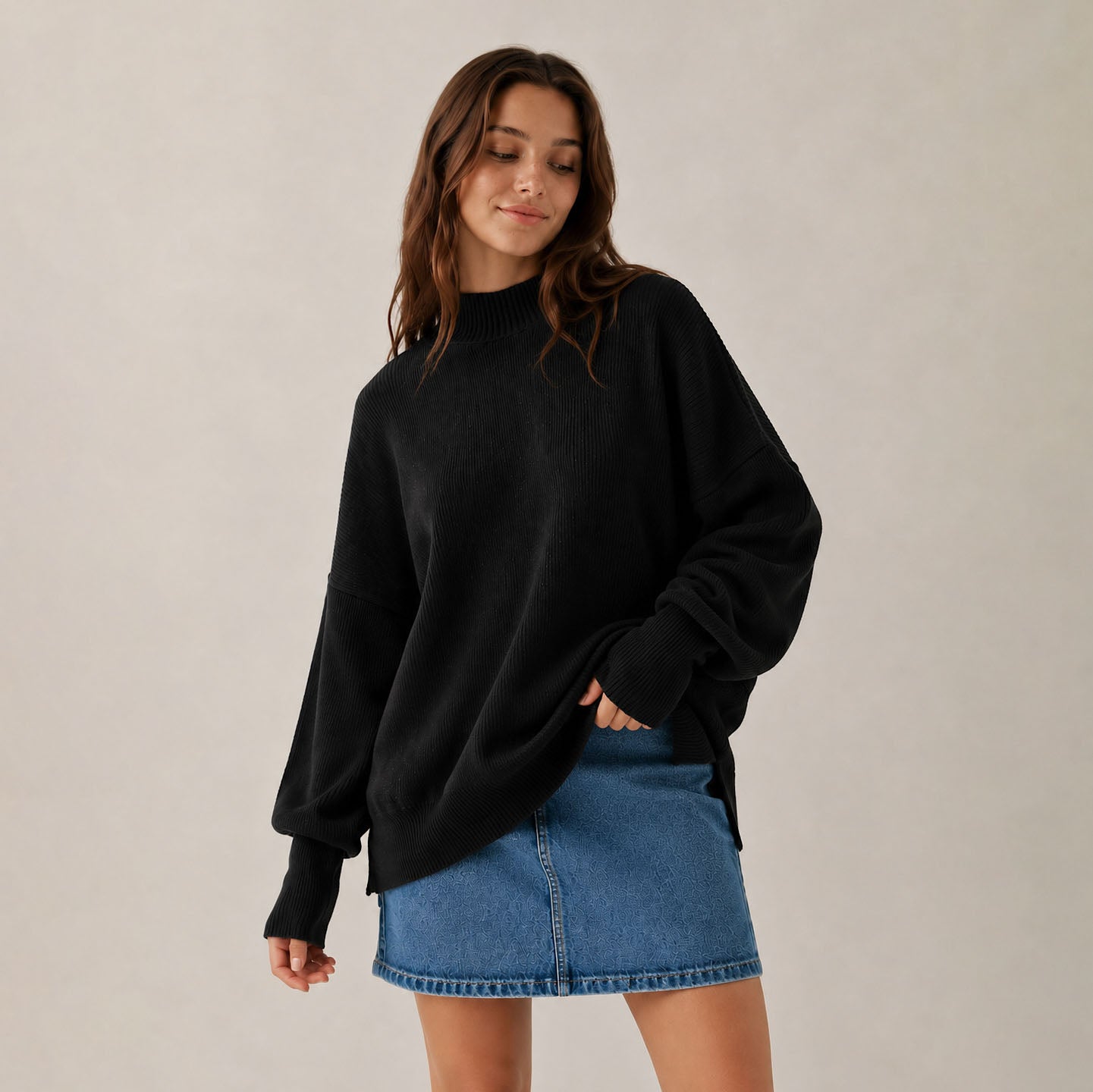 Woman wearing a black oversized sweater and blue denim skirt on a plain background