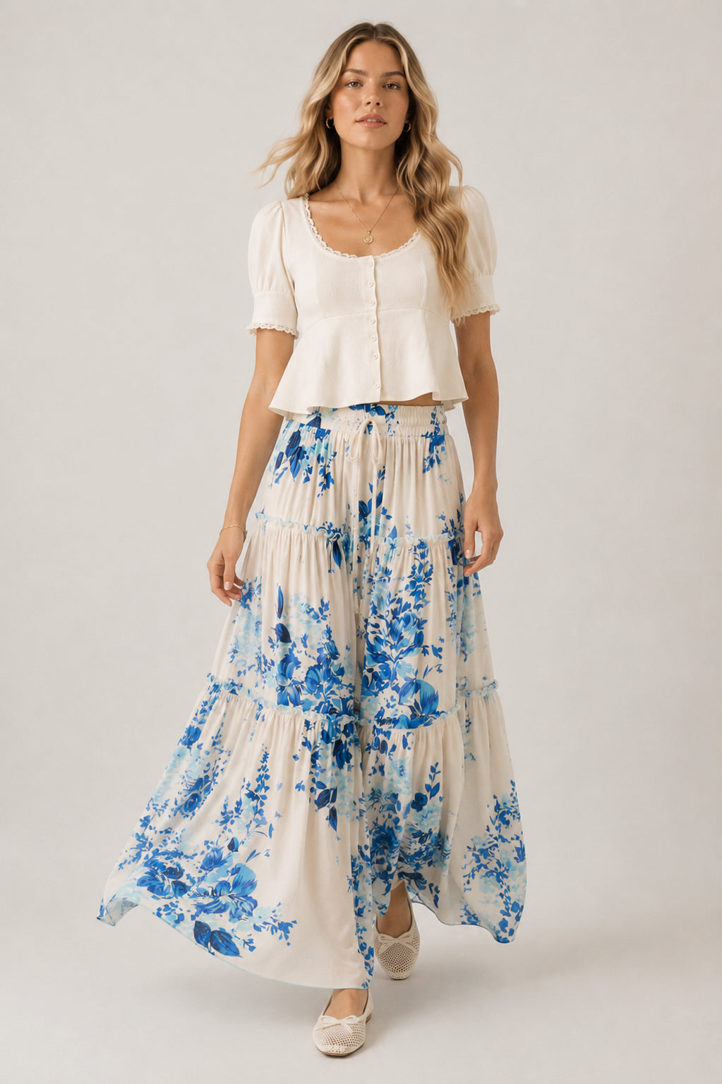 Woman wearing a white top and blue floral skirt on a plain background
