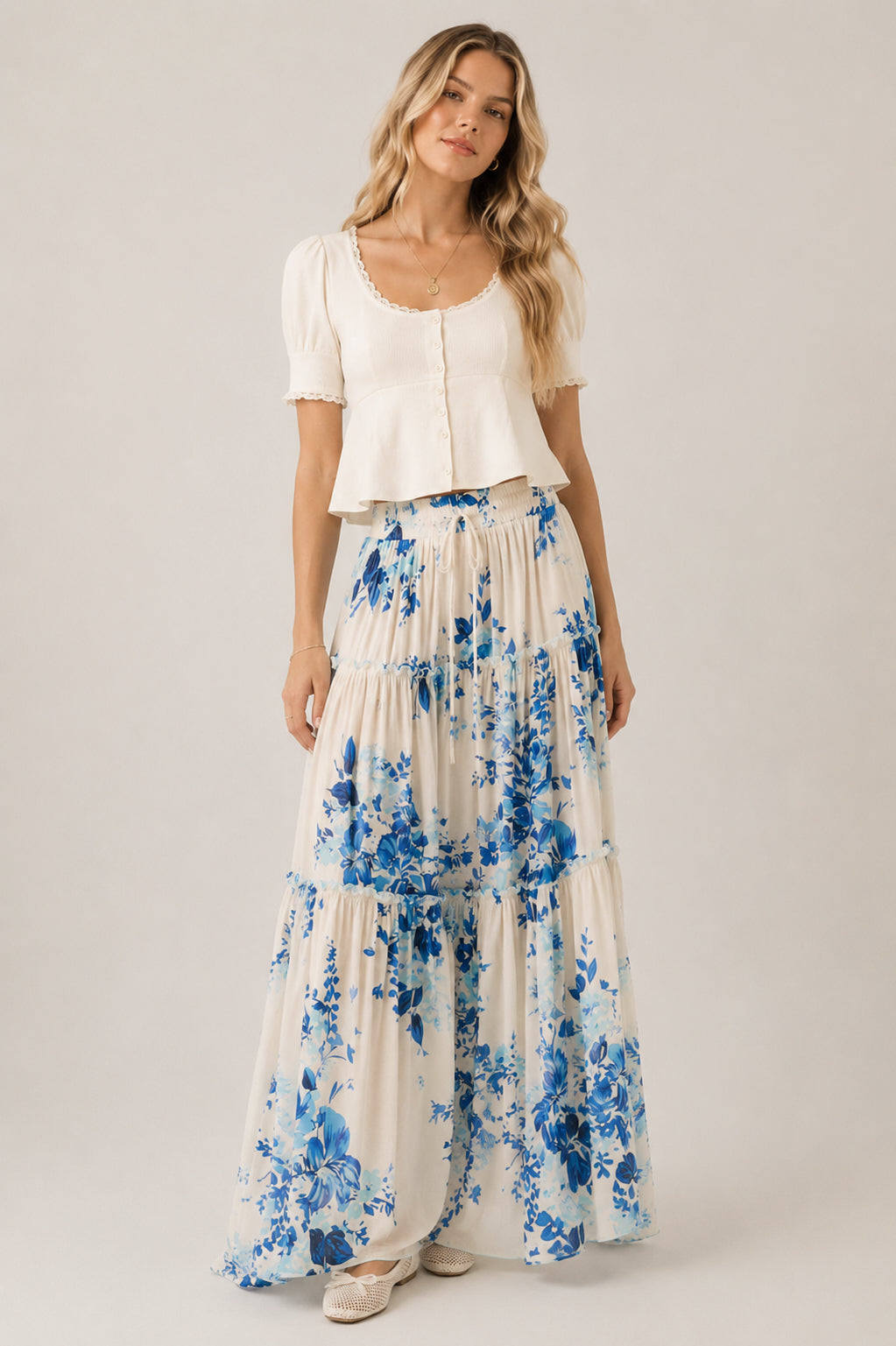 Woman wearing a white top and blue floral skirt on a plain background