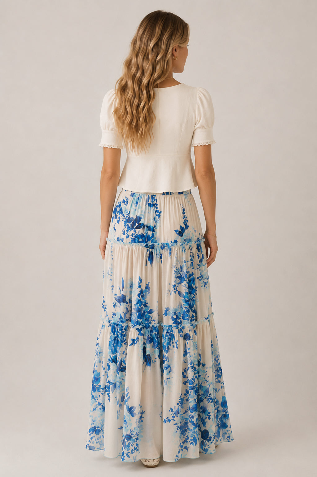 Woman wearing a white top and blue floral skirt on a plain background