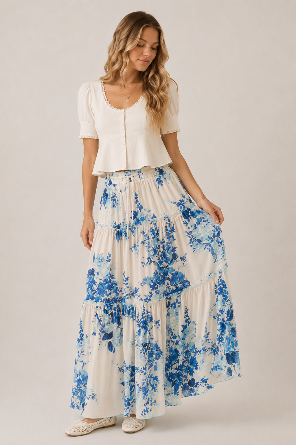 Woman wearing a white top and blue floral skirt on a plain background