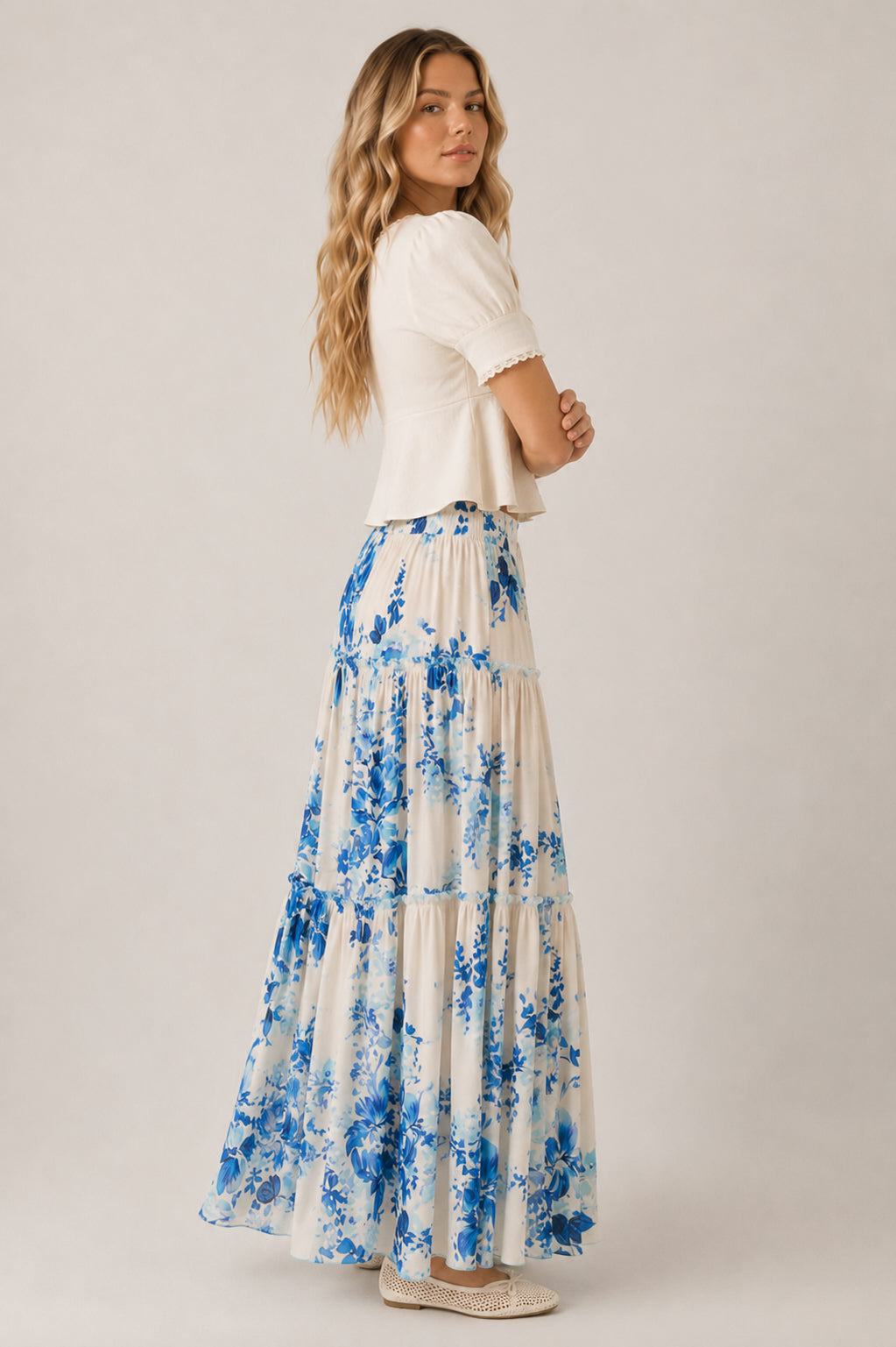 Woman wearing a white top and blue floral skirt on a plain background
