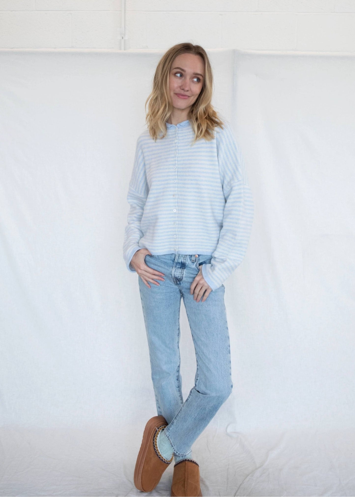 Woman wearing a light blue striped sweater and jeans against a white background