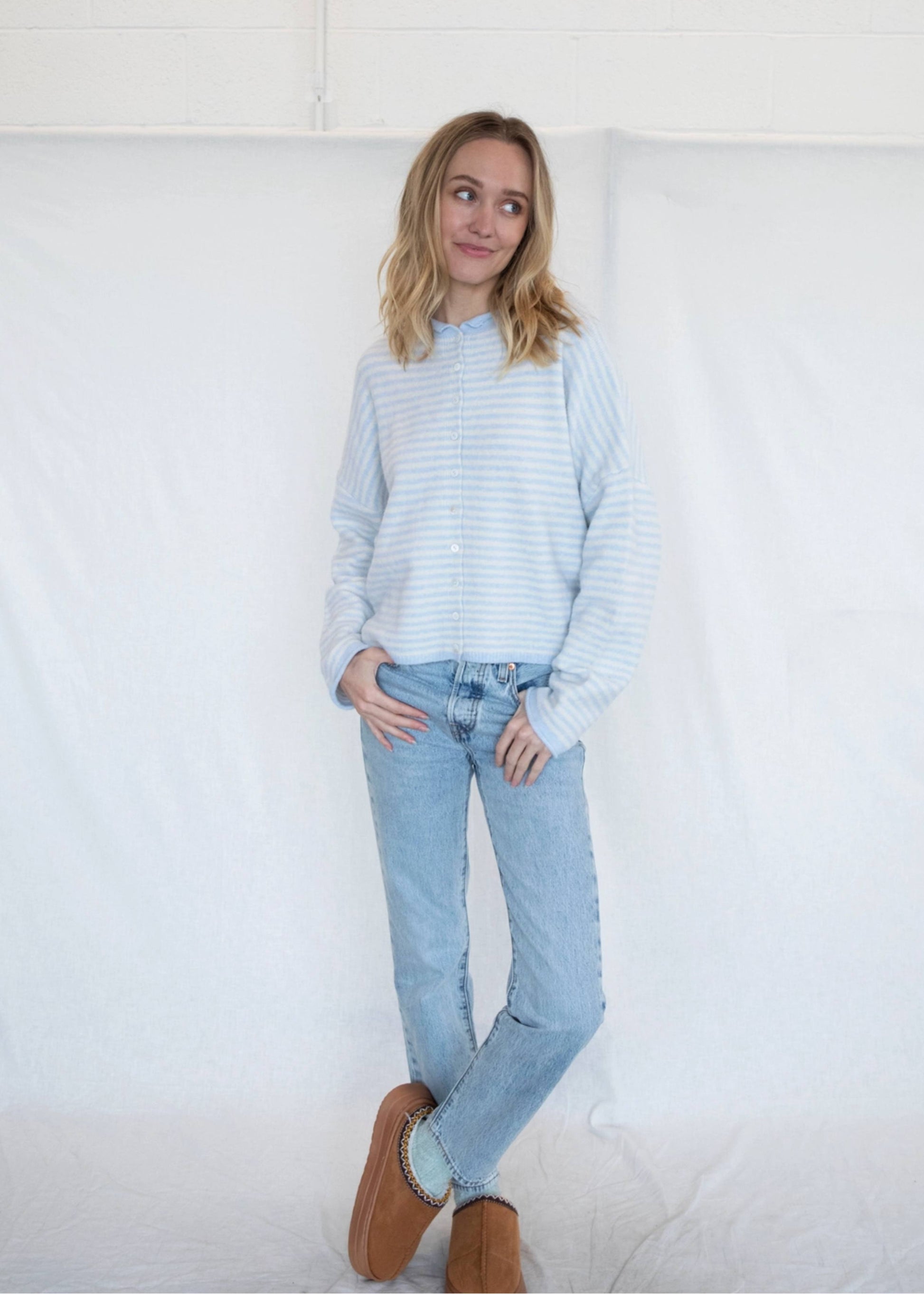Woman wearing a light blue striped sweater and jeans against a white background