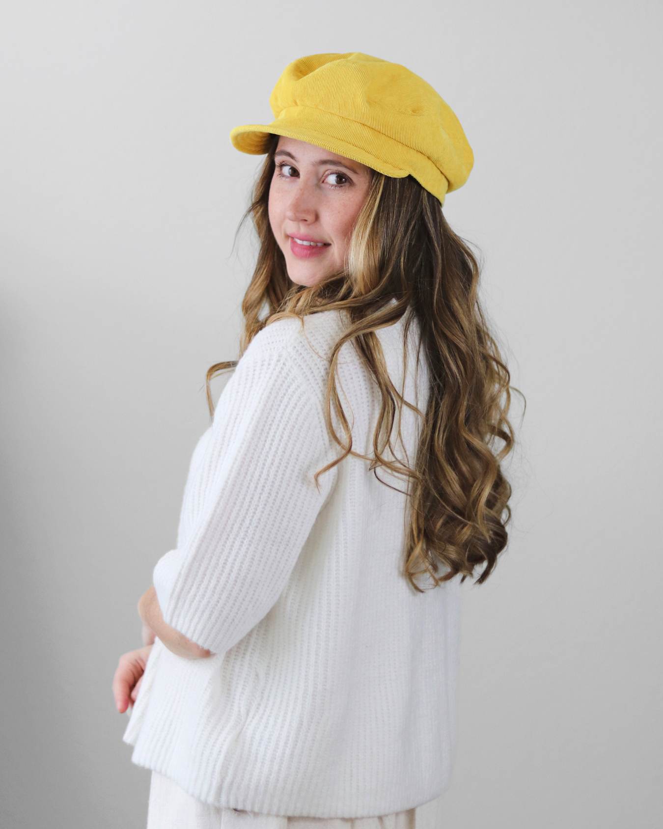 Woman wearing a yellow cap and white sweater against a plain background
