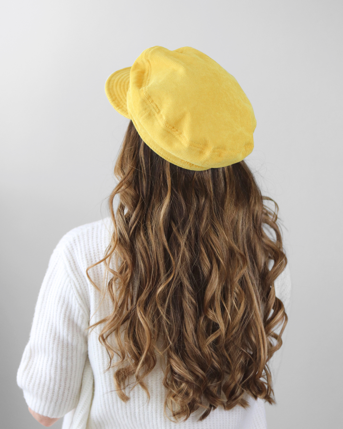 Person wearing a yellow beret with long wavy hair on a plain background