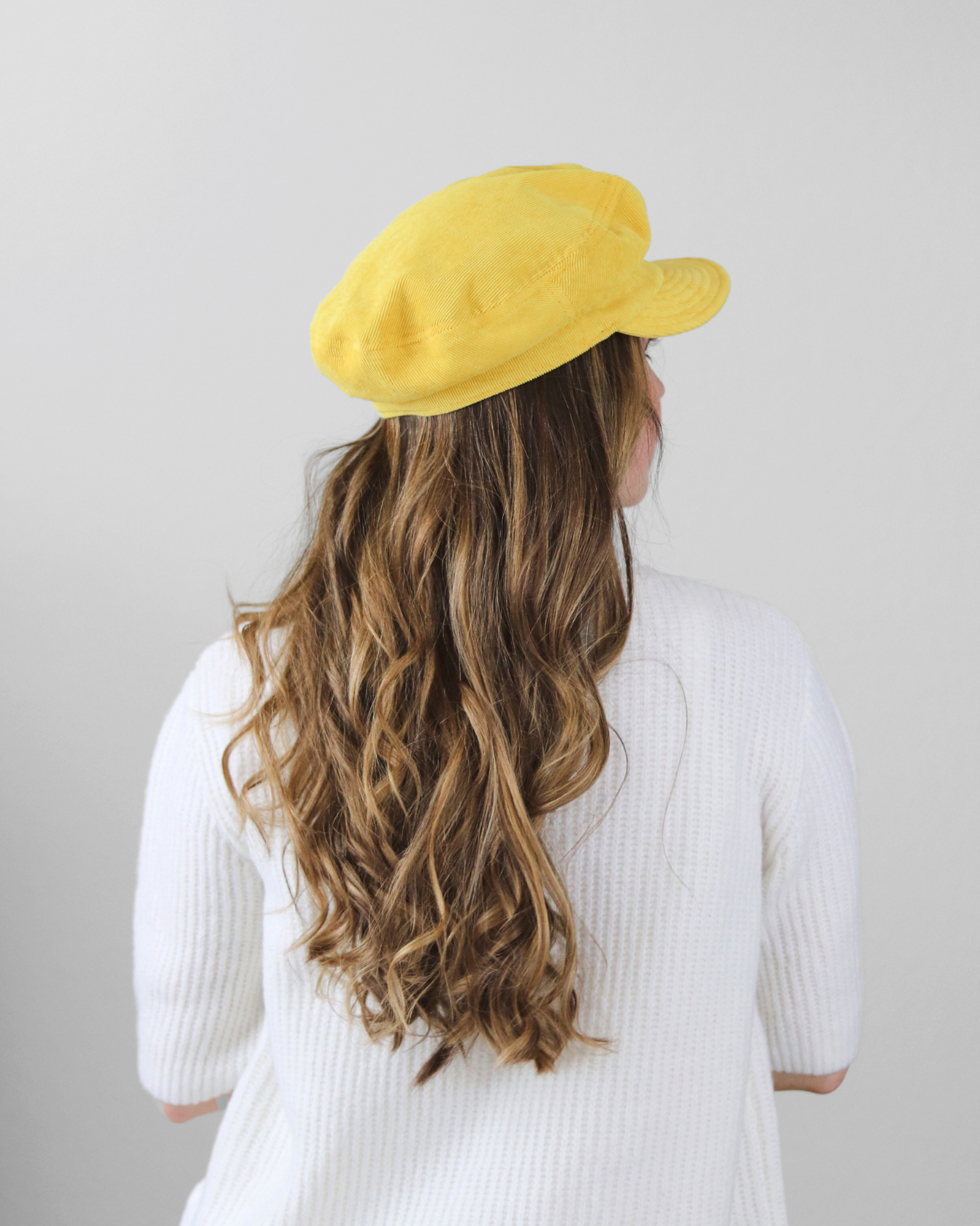 Person wearing a yellow beret with long, wavy hair on a plain background