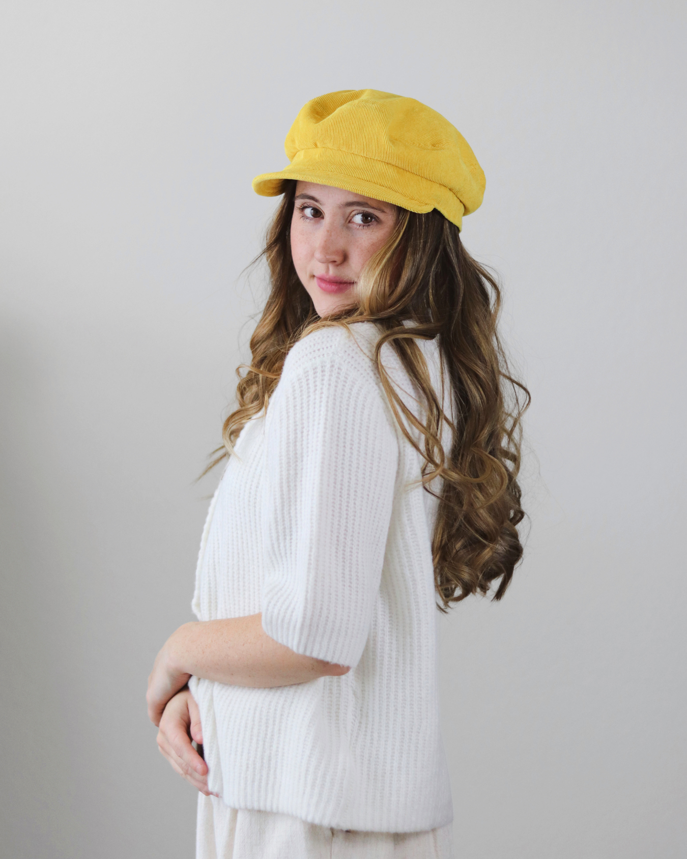 Woman wearing a yellow cap and white sweater against a plain background
