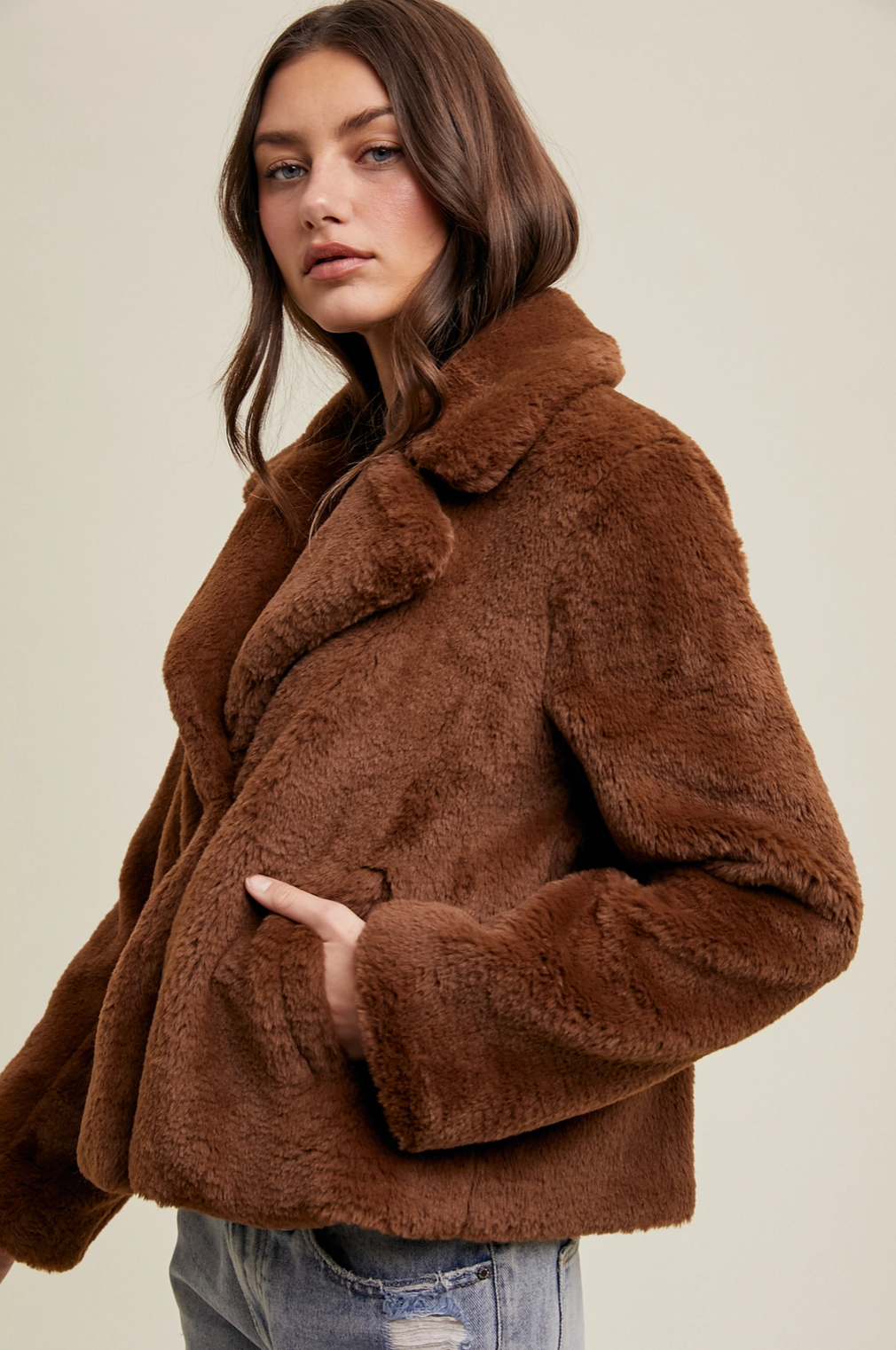 Woman wearing a short chocolate brown faux fur jacket featuring a cozy oversized texture, side pockets, and a classic winter outerwear silhouette.