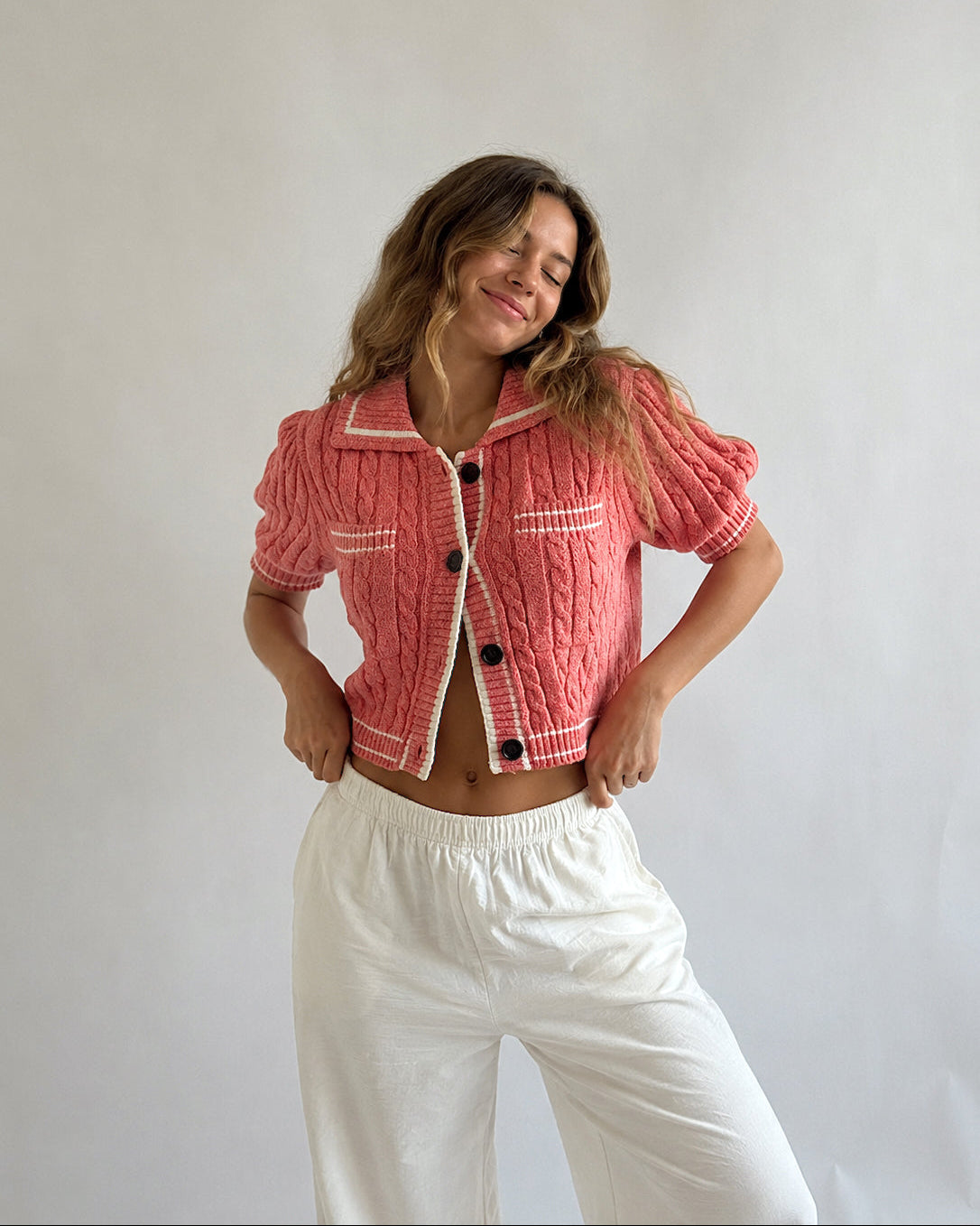 Woman wearing a pink textured jacket with white trim and white pants against a plain background