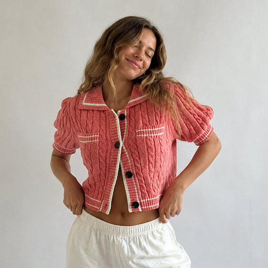 Woman wearing a pink textured jacket with white trim and white pants against a plain background