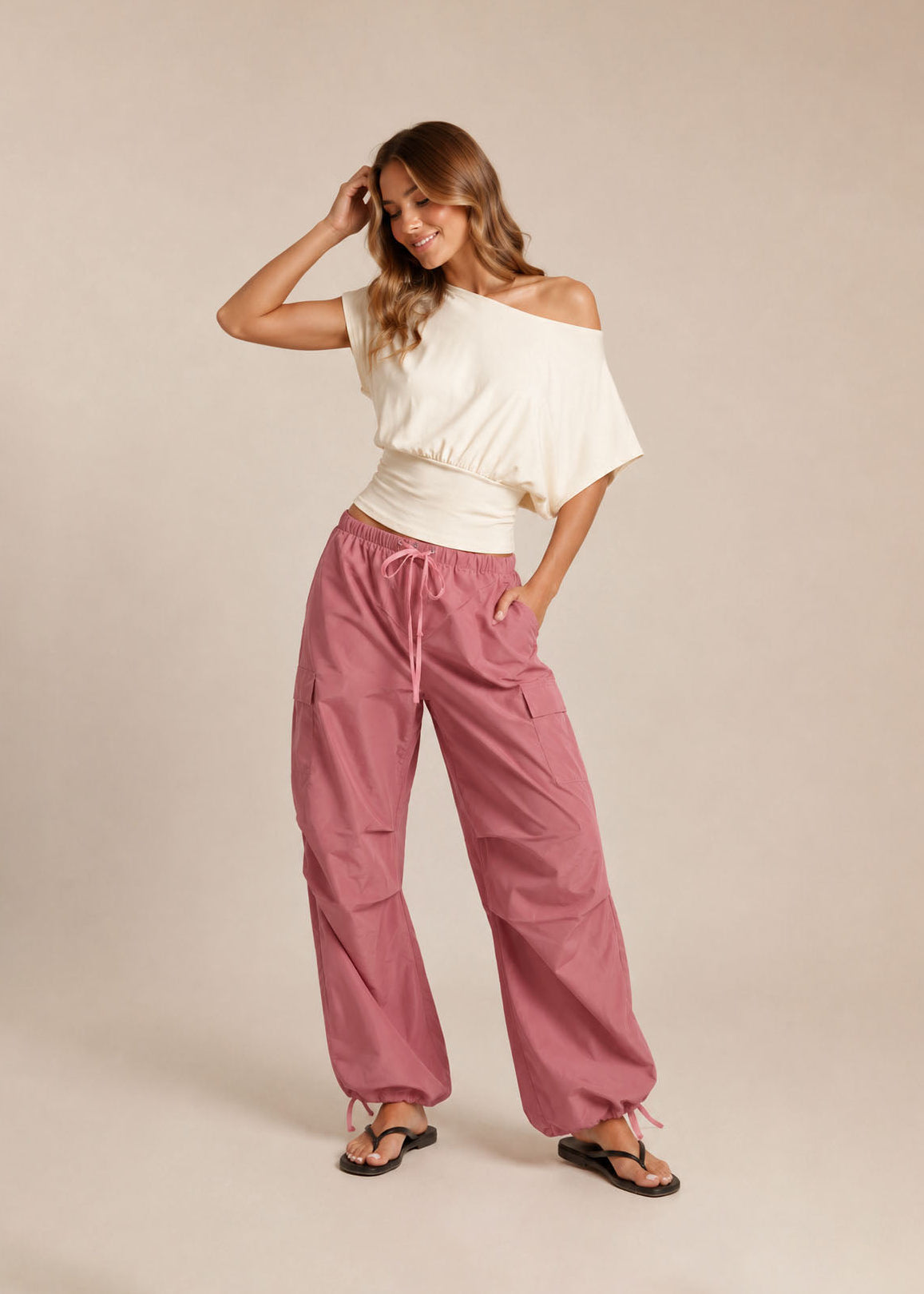 Woman wearing a white off-shoulder top and pink pants on a beige background