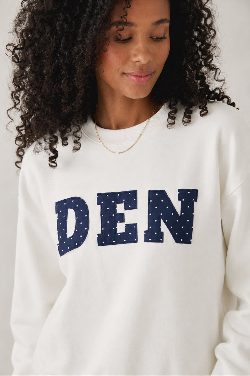Person wearing a white sweatshirt with 'DEN' printed on it against a plain background
