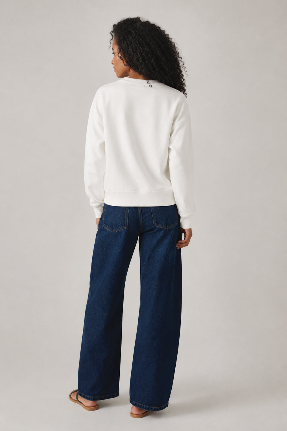 Person wearing a white sweater and blue jeans on a plain background