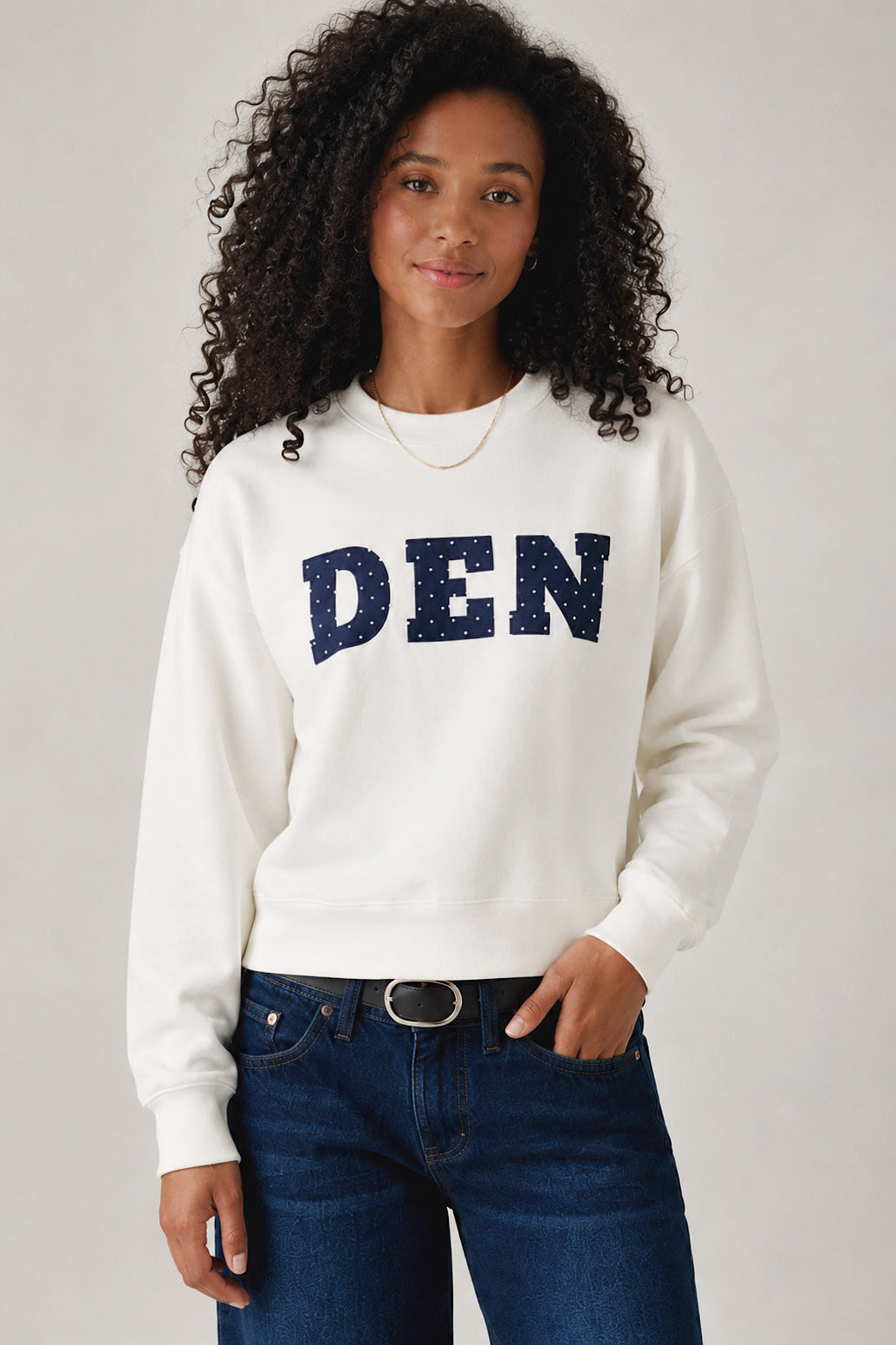 Person wearing a white sweatshirt with 'DEN' printed on it against a plain background