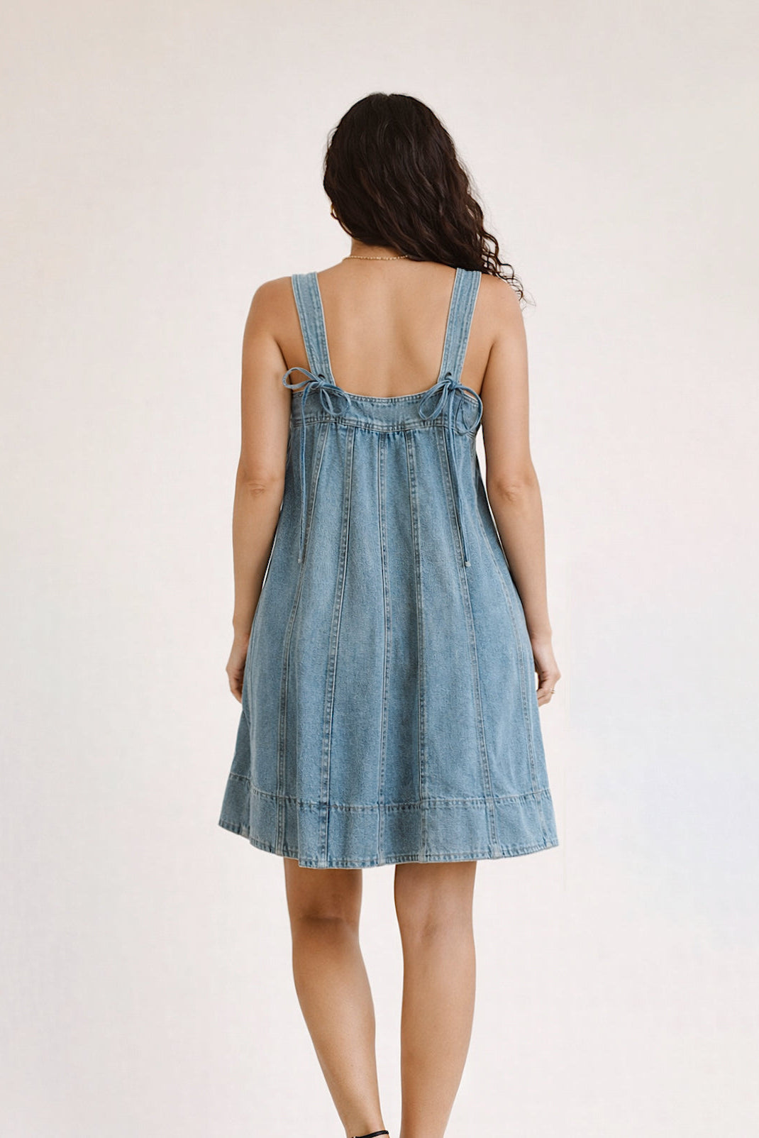 Woman wearing a denim dress with thin straps on a plain background