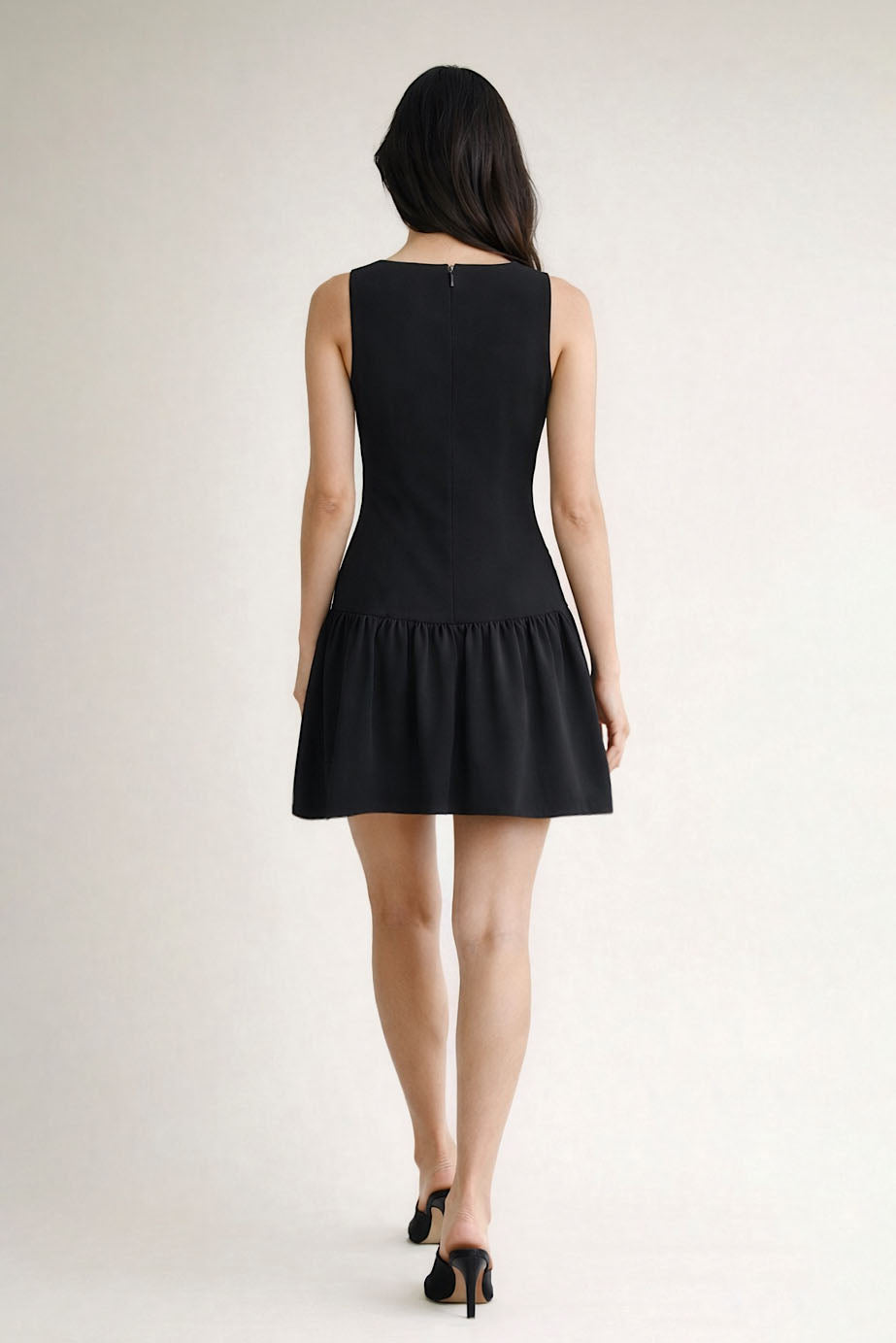 Woman wearing a black sleeveless dress on a plain background