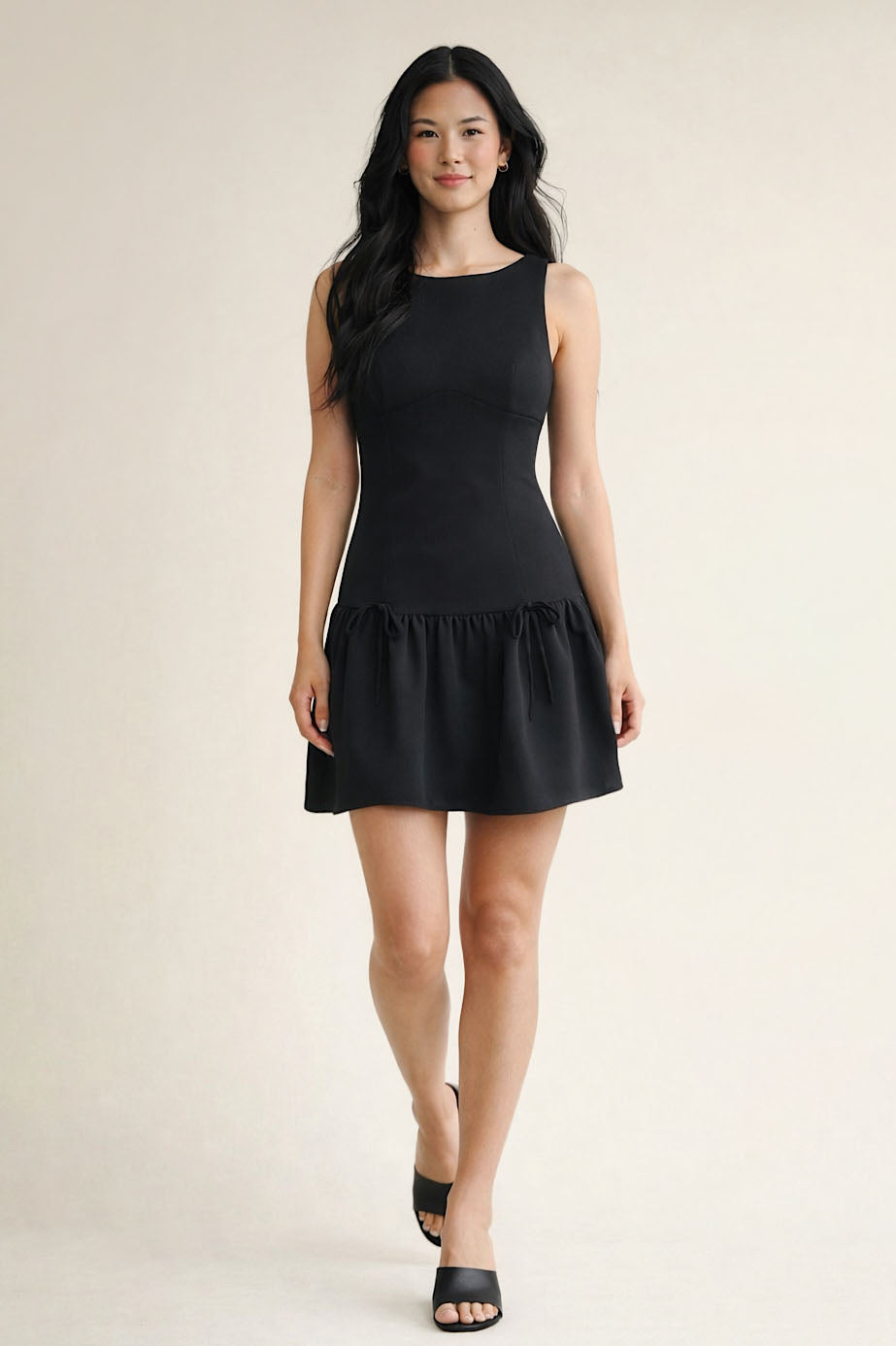 Woman wearing a black sleeveless dress against a plain background