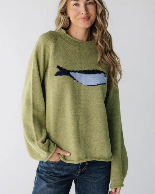 Woman wearing a green sweater with a whale design on a plain background