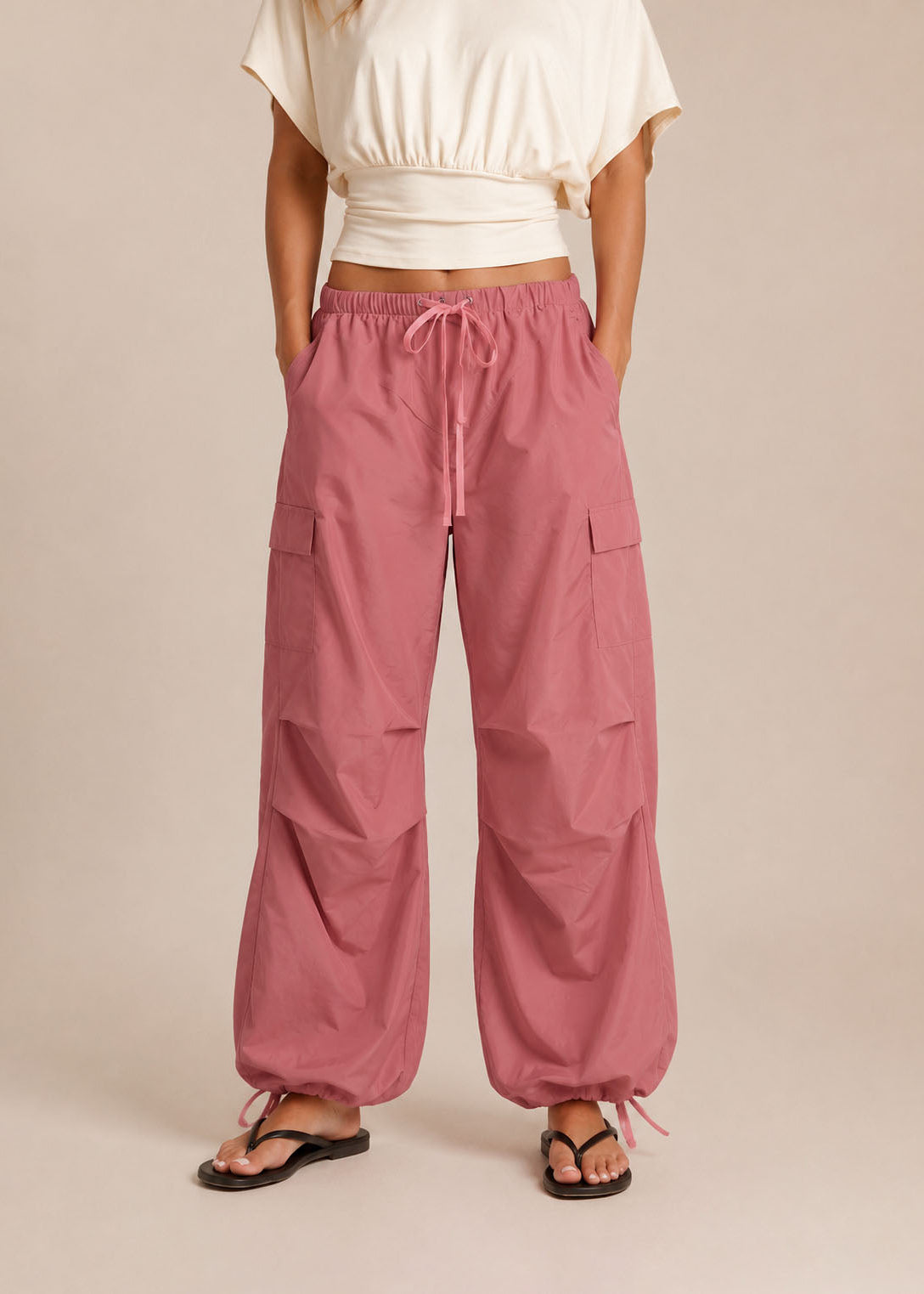 Person wearing pink cargo pants and a white top on a beige background