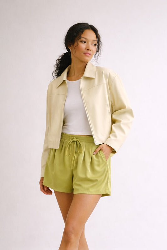 Woman wearing a beige jacket, white top, and green shorts on a plain background