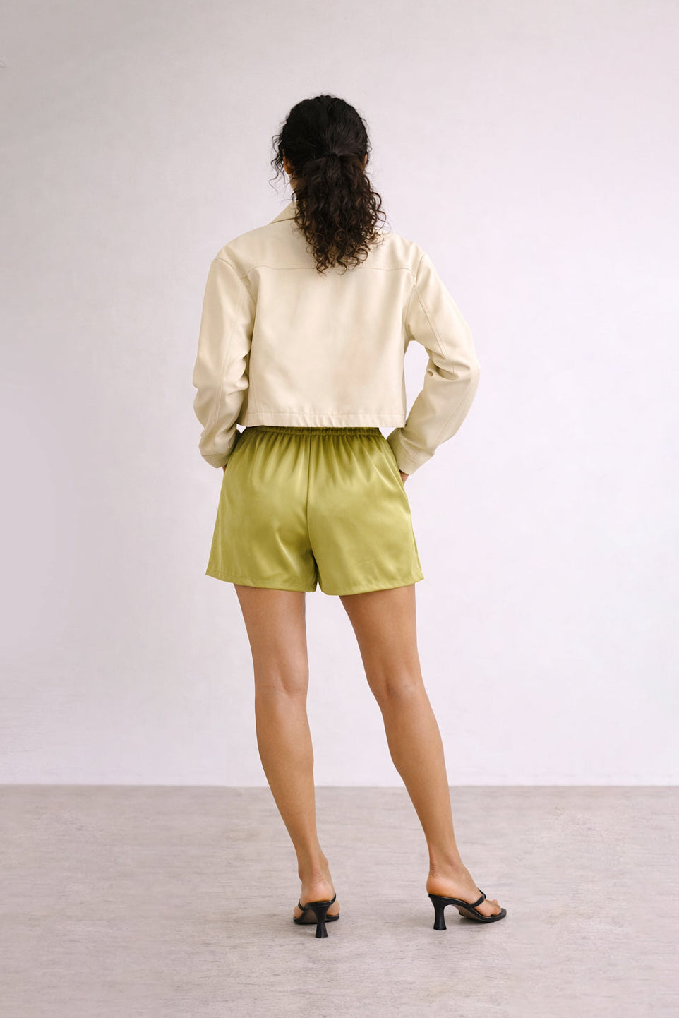 Person wearing a cream jacket and green shorts on a plain background