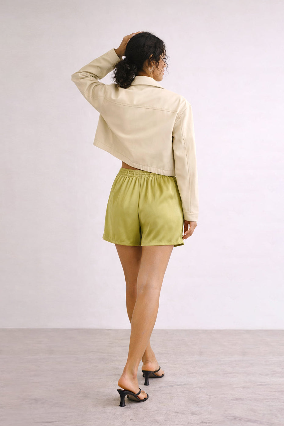 Person wearing a beige jacket and green shorts against a white background