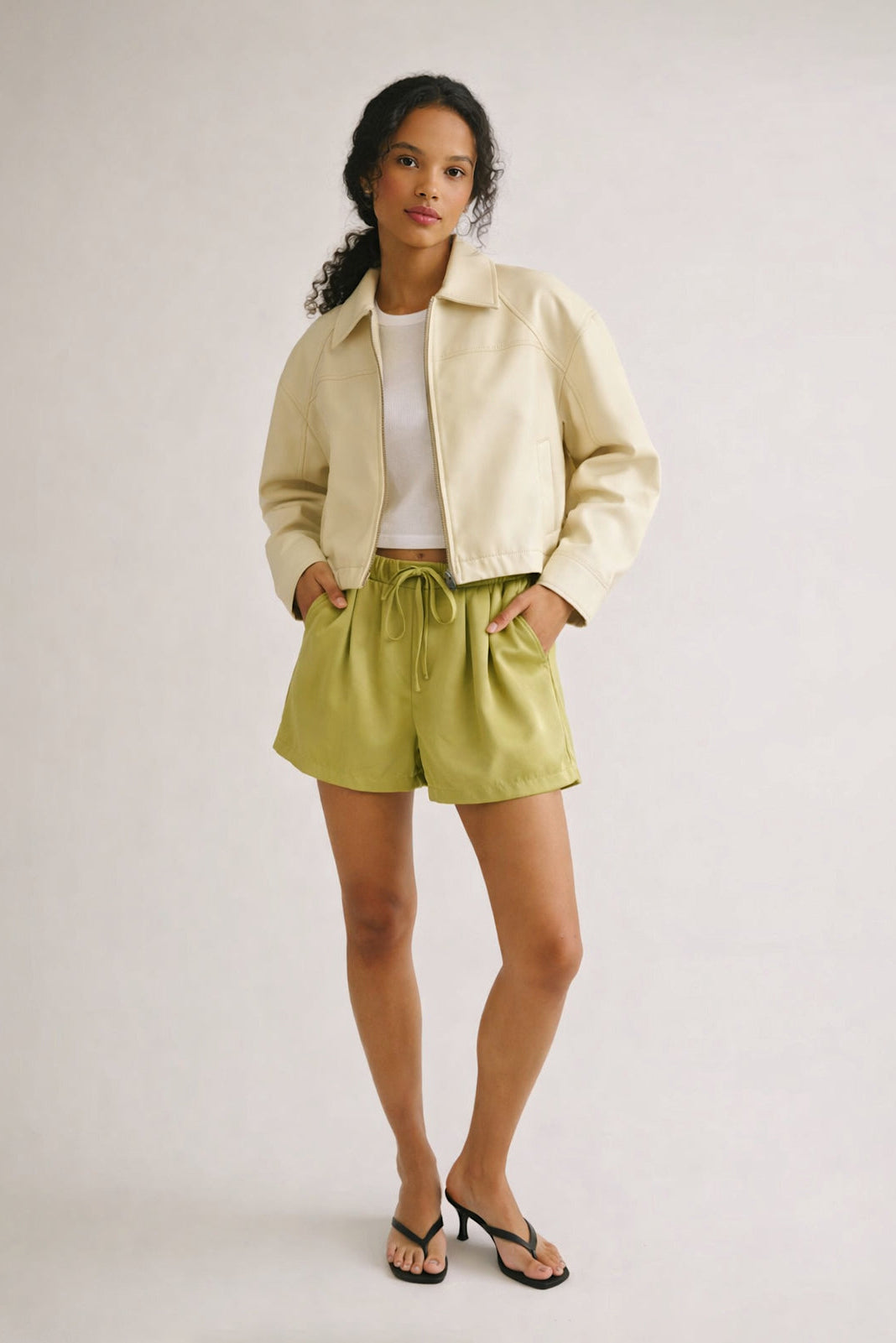 Woman wearing a light-colored jacket and green shorts on a plain background