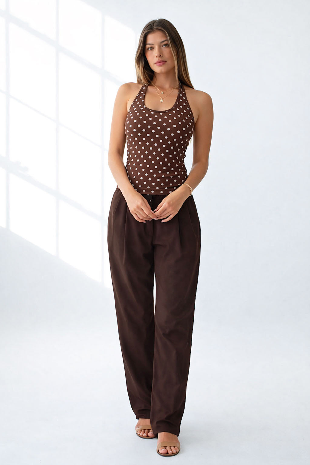 Woman wearing a brown polka dot top and wide-leg pants on a white background