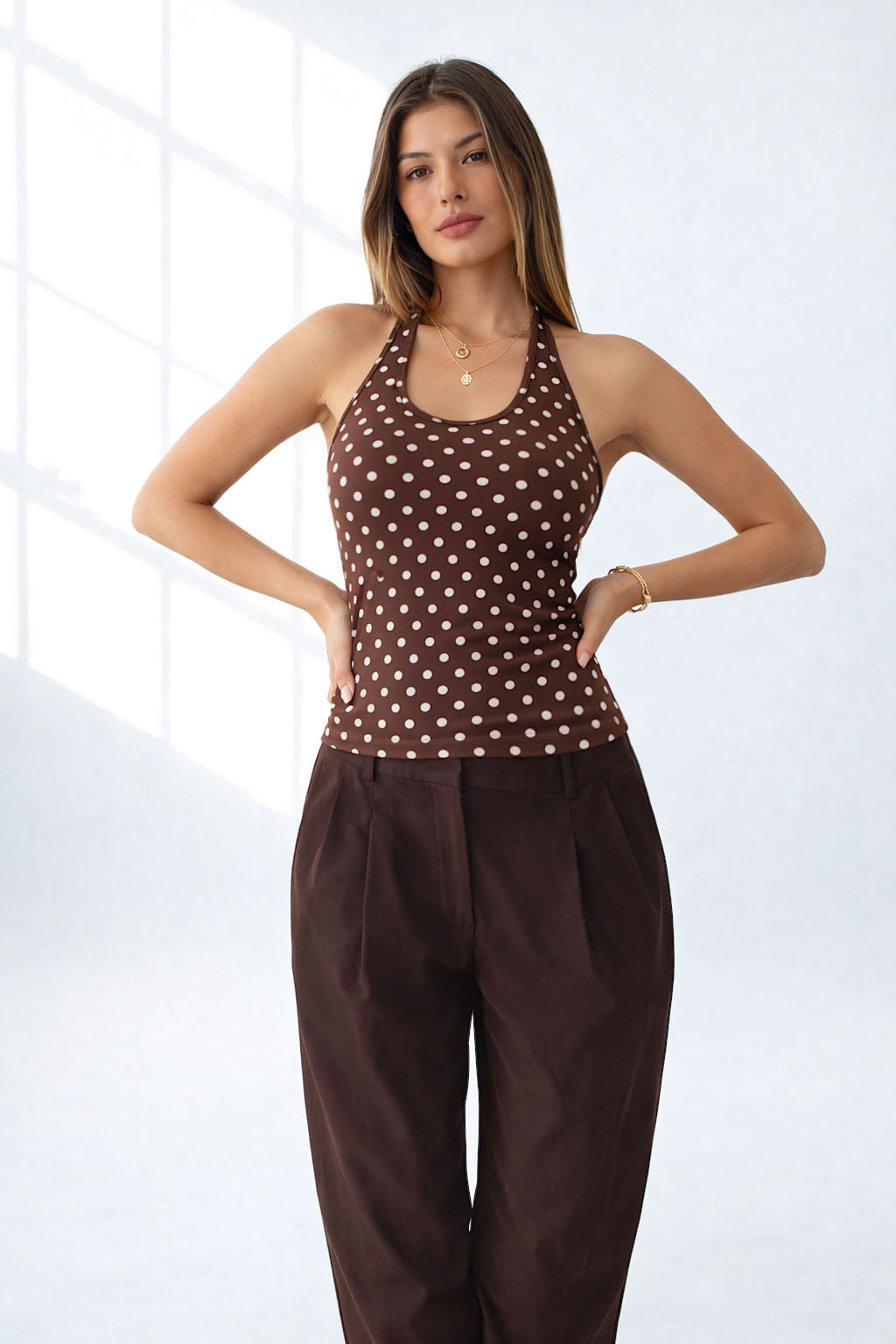 Woman wearing a brown polka dot top and wide-leg pants on a white background