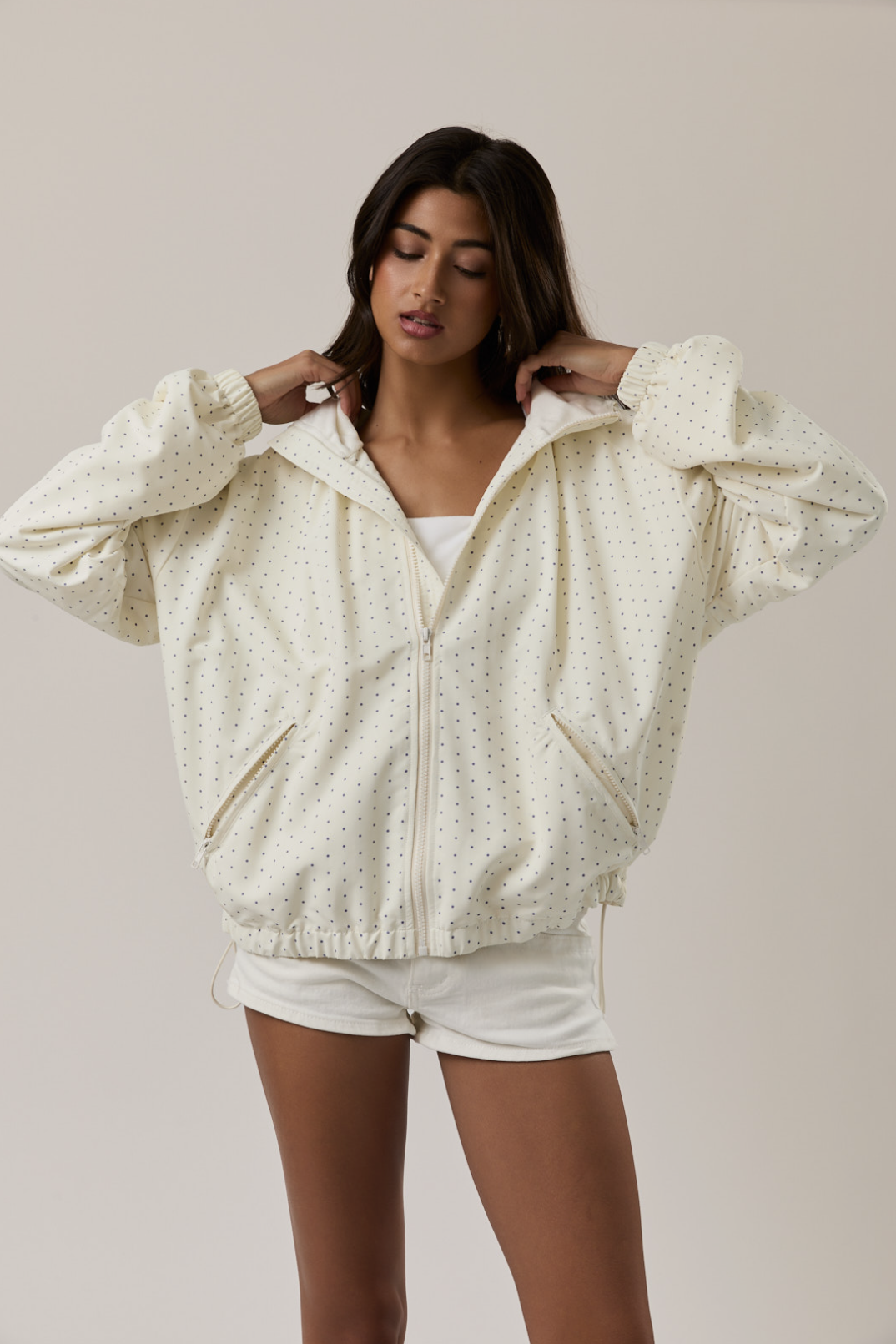 Woman wearing a light-colored zip-up hoodie and white shorts against a plain background