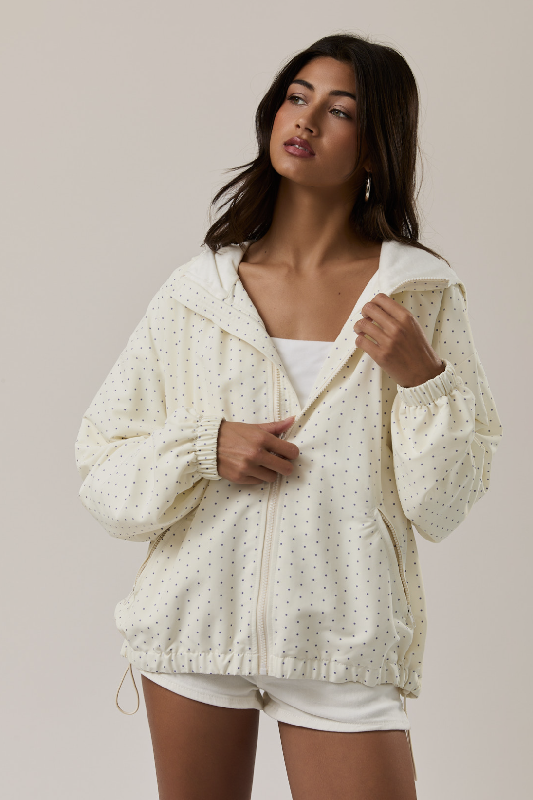 Woman wearing a cream-colored lace jacket over a white top and shorts on a plain background