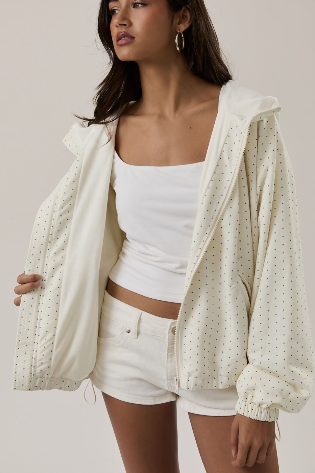 Woman wearing a white top and shorts with a patterned beige jacket on a plain background
