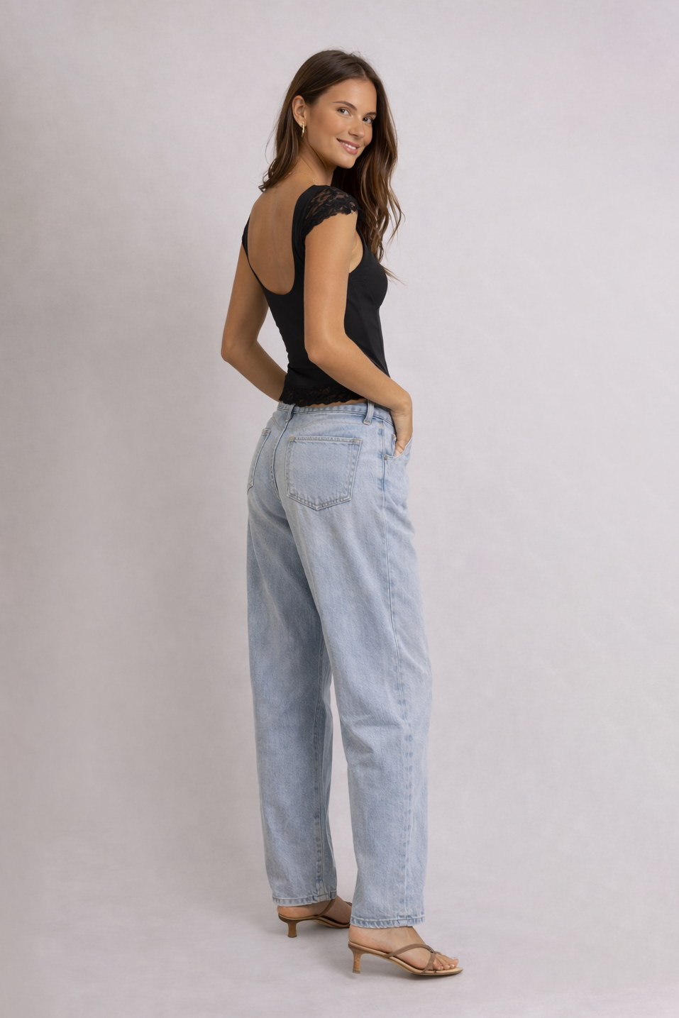 Woman wearing a black sleeveless top and light blue jeans on a plain background