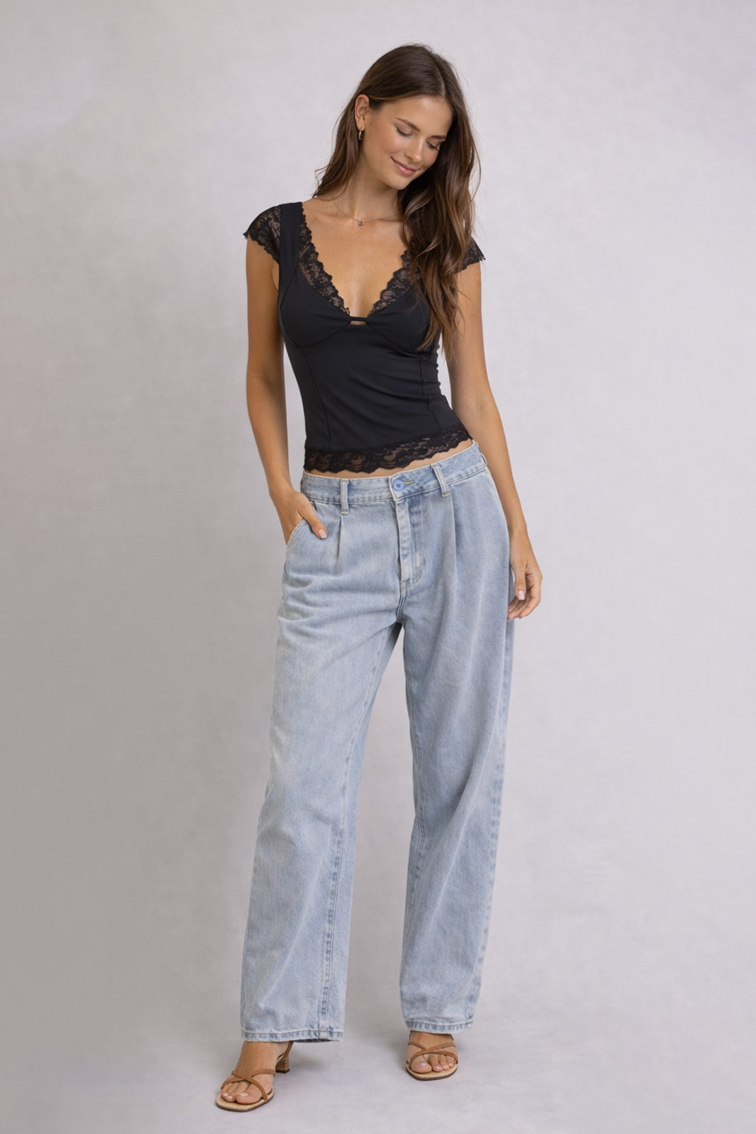 Woman wearing a black lace top and light blue jeans on a plain background