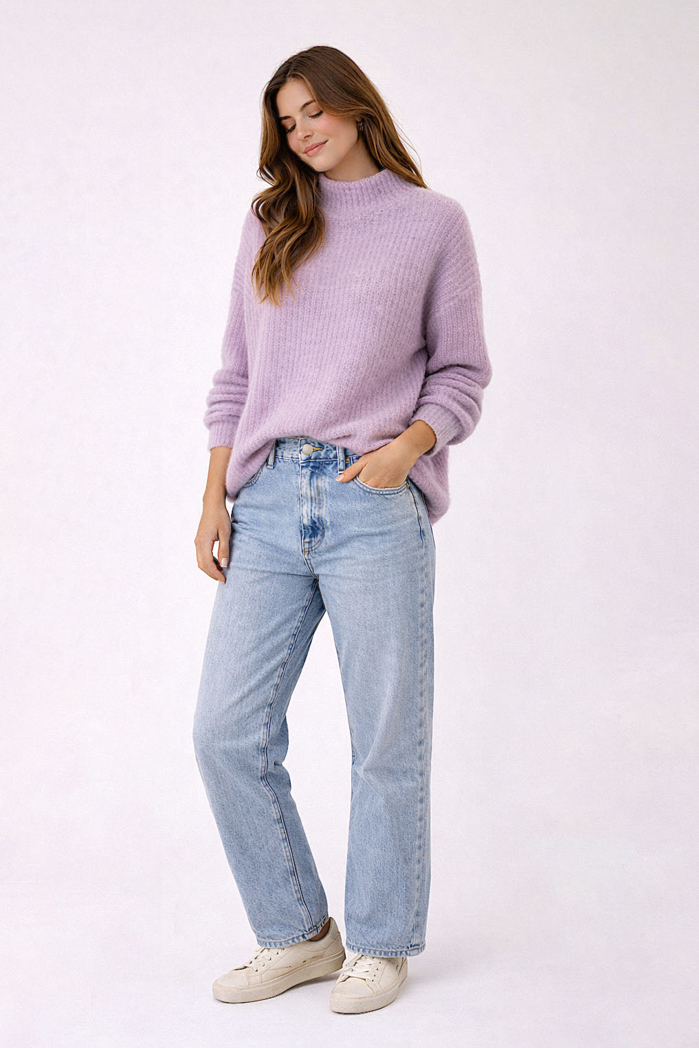Woman wearing a lavender sweater and light blue jeans on a white background