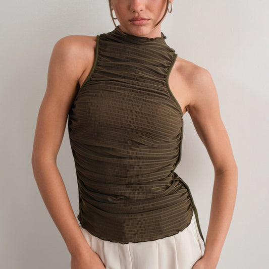A person wearing an olive green high neck ruched tank top with a lettuce-edge mock neck and low-cut armholes, paired with a white skirt.